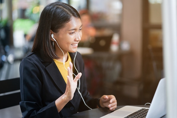 close up asian woman use earphone connect to laptop and talking greeting by video conference with friends or family at outdoor coffee restaurant in relax time , lifestyle people concept
