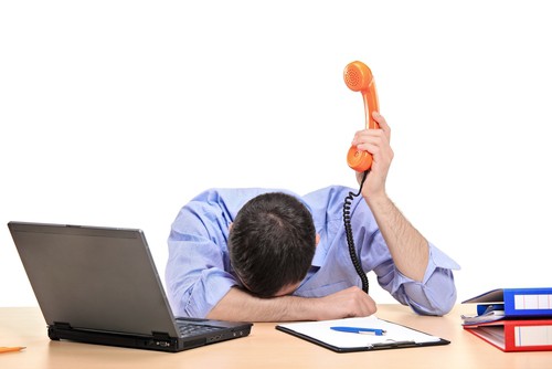 a picture of a frustrated male holding the phone above his head with his head down with a laptop next to him.